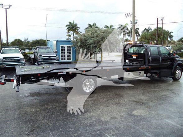 Tow truck with flatbed and black cab, rear wheel view, some text on side panels is not legible.