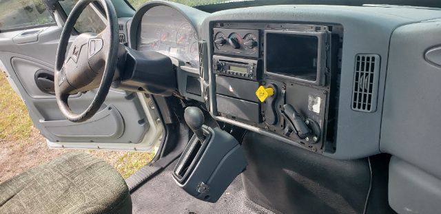Cab and chassis interior showing steering wheel, dashboard with gauge cluster, aftermarket radio, and a touchscreen display panel missing from center, yellow warning tag, and gear selector.