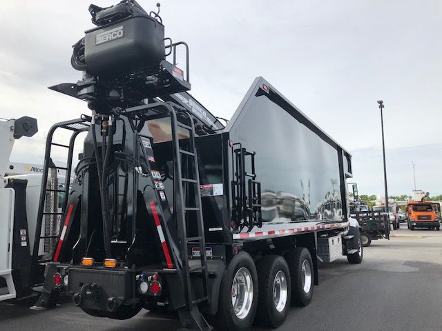 Freightliner 114SD grapple truck with a mounted crane and a reflective dump bed, rear view showing triple axle wheels and equipment on the back.