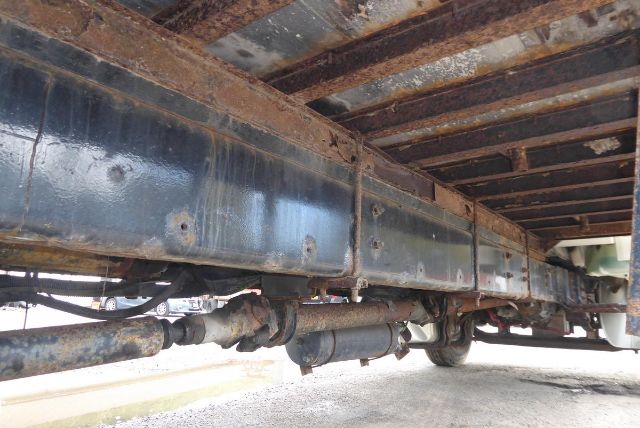 Underbody view of a Freightliner M2 106 trailer frame showing the chassis rails, drivetrain components, and undercarriage with some rust and wear.