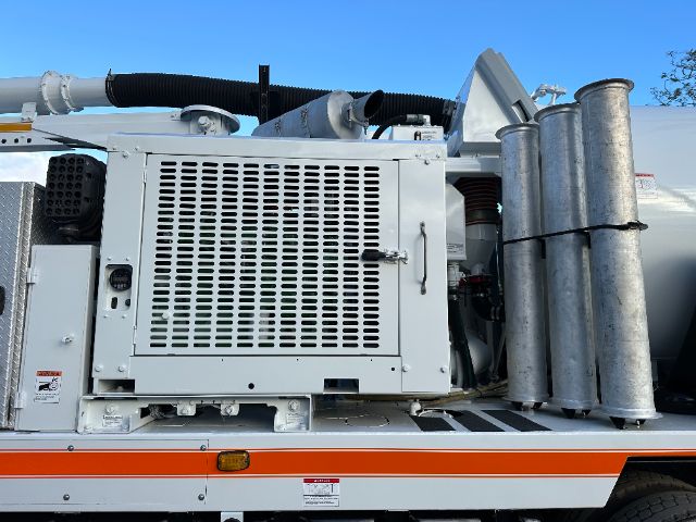 Truck vacuum unit with large radiator-like panel, exhaust stacks, and metal tubes on side; visible hoses and control panel.