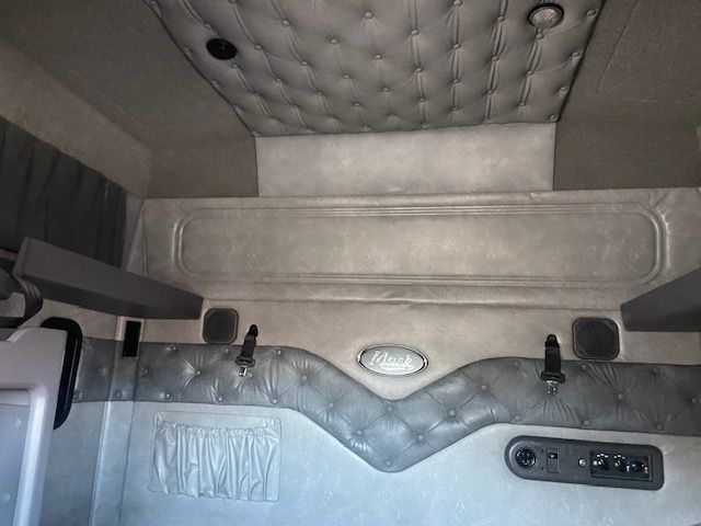 Truck cab sleeper interior with quilted upholstery, metal rear wall, and control panel on the side.()