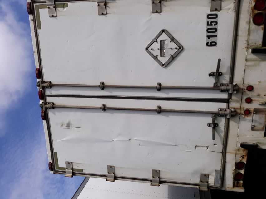 Rear view of a white utility trailer with double doors, door hinges, latches, and a diamond-shaped hazard placard. trailer number 61050 visible on lower right.