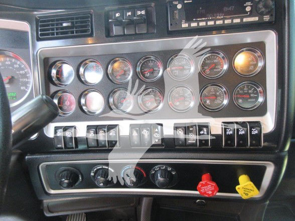 Dashboard gauges and switches of a Kenworth W900L truck showing multiple round gauges, switches, and control knobs in a metallic console.