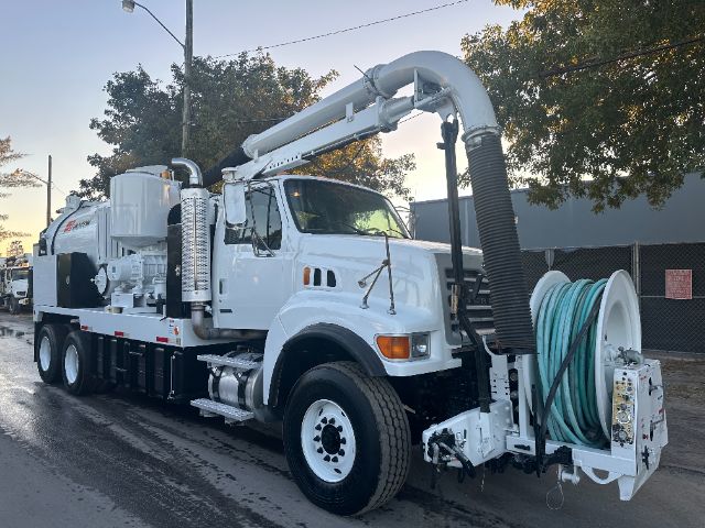 Vacuum truck with large hose reel and boom, white cab and body, rear hose reel equipment, side steps, dual rear wheels.