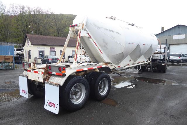 Trailer rear view of a Fruehauf dry bulk pneumatic trailer with silver tank, dual rear axles, mud flaps, and white reflective markings.