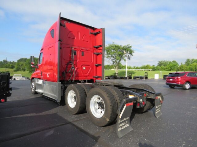 Freightliner Cascadia Evolution truck chassis and rear section viewed from behind, red cab with sleeper, dual rear axles and fifth wheel missing, dealership lot in background.