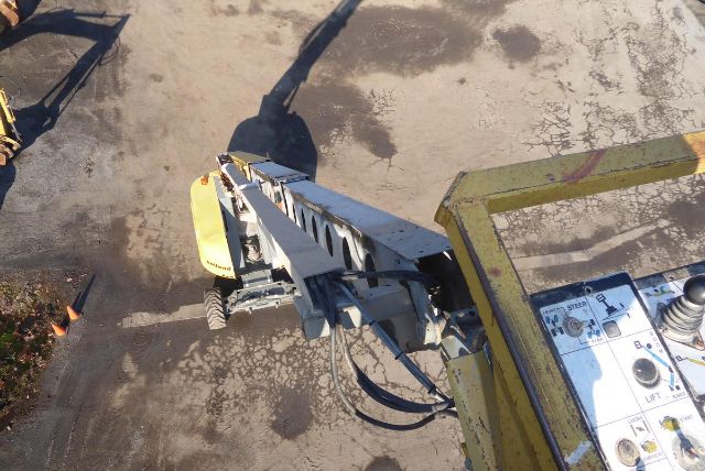 Grove T60 boom lift viewed from operator platform with yellow railing and control panel overhead, showing hydraulic hoses and base on concrete.