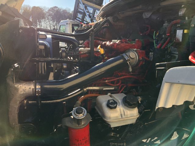 Freightliner M2 engine bay with red engine block, black intake pipe, white coolant reservoir, and various hoses and components visible.