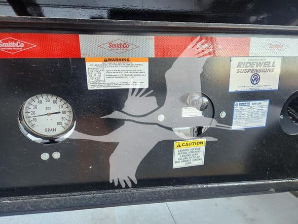 SmithCo equipment panel showing a gauge, warning labels, and a silhouette graphic. Gauge reads 0-150 psi with unit 'PSI' and 'SPAN'. Labels include 'SmithCo' branding, warning sticker, and 'Ridewell Suspensions' sticker.