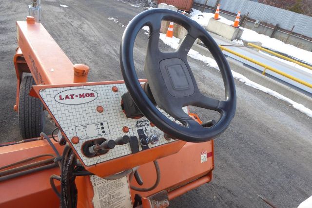 Laymor SM300 trucking equipment steering wheel and control panel showing Lay-Mor branding and control levers in orange chassis.