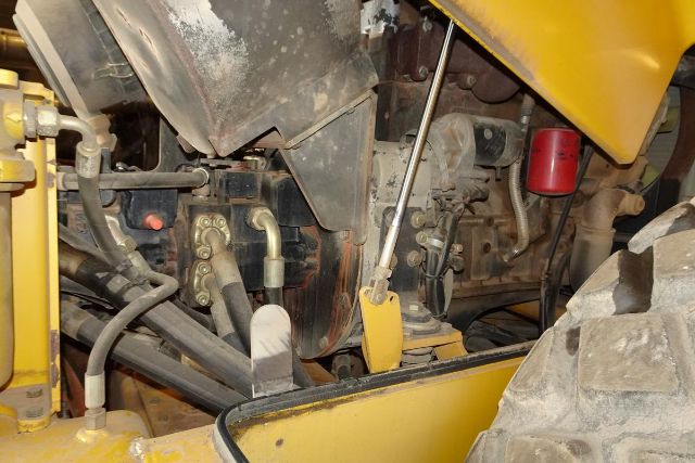 Vehicle engine bay of Vibromax VM106D with hydraulic lines, levers, and yellow exterior visible.