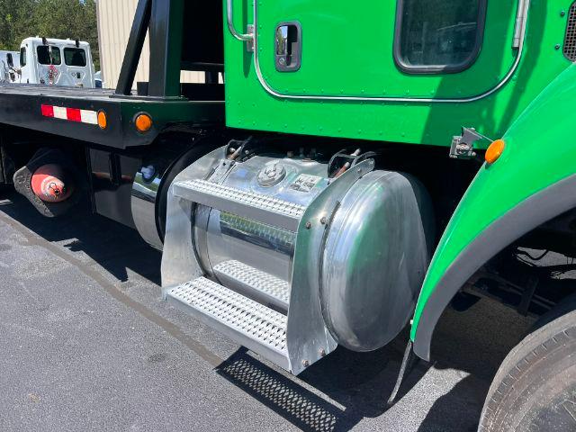 Fuel tank on green Peterbilt 348 truck with side steps and rear rollback equipment.