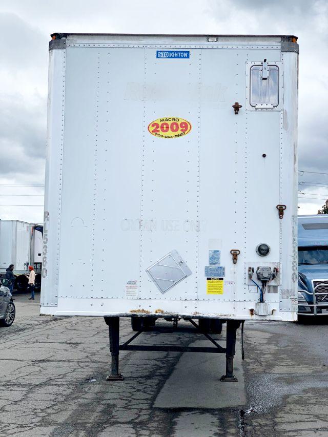 Back view of a white 2009 Stoughton dry van trailer on gooseneck legs showing Stoughton logo and safety decals.