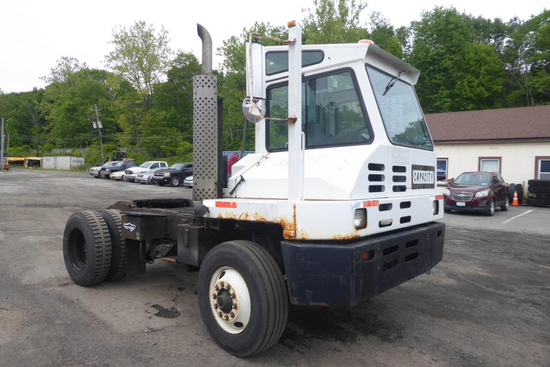 Truck cab with white body and black bumper showing large exhaust stack; front-right view, Gravity  Daniel label; visible rust along frame and panel gaps.