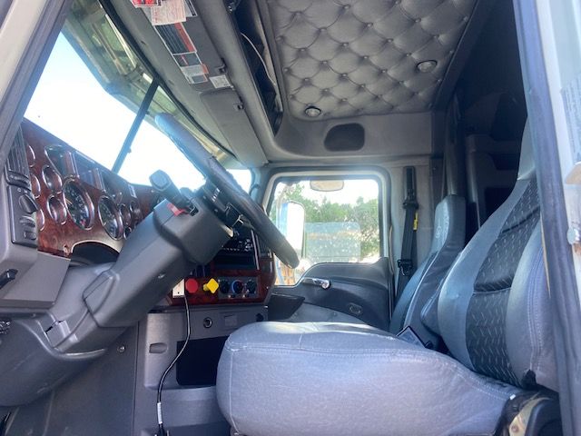 Truck cab interior of a 2015 Mack CXU613 with plaid seats, steering wheel, dashboard gauges, and sleeper area visible