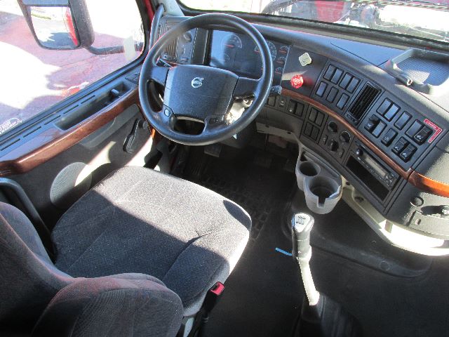 Volvo truck sleeper cab interior showing steering wheel, dashboard with gauges, gear shifter, cup holders, and driver seat.
