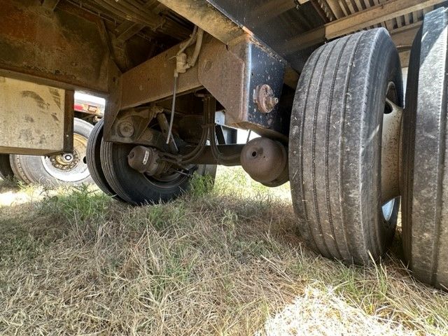 Trailer undercarriage showing dual rear axles and leaf springs; undercarriage beams and tire set visible.