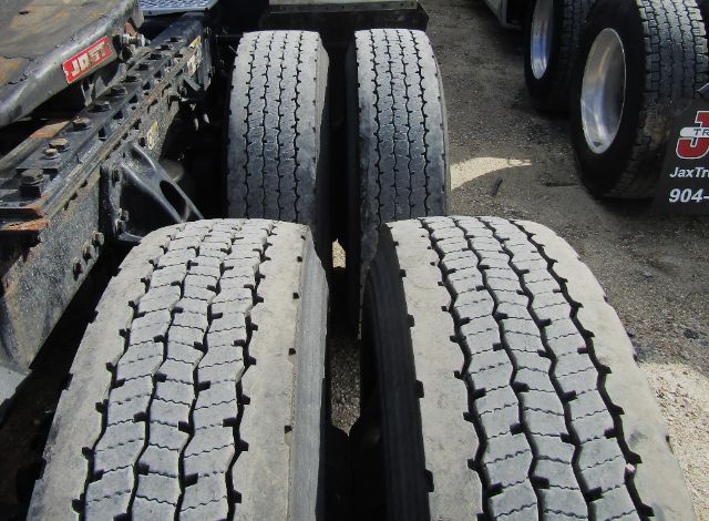Kenworth T680 truck chassis with dual rear axles and multiple large tires visible in a yard.