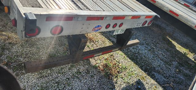 Rear view of a used flatbed trailer showing stamped metal, taillights, and reflective tape. Visible are bumper, license plate area, and a small sticker with blue and red graphics.