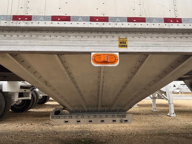 Aluminum sand/grain hopper trailer underside with center loading hopper and small orange rear clearance/marker light.