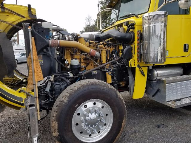 Peterbilt 389 engine bay with exposed diesel engine, yellow truck cab, chrome air intake, and large front wheel visible.