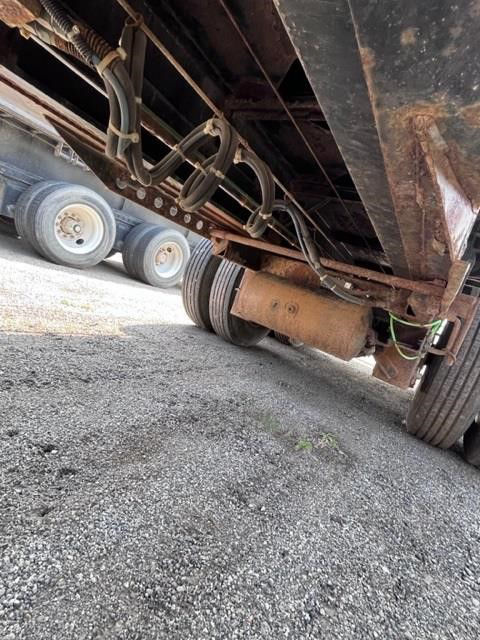 Underneath view of a 2002 Manac steel flatbed trailer showing suspension, axle, and undercarriage components including water/dust hose and frame.