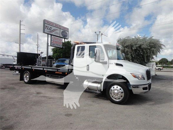 International MV tow truck with a flatbed, white cab, chrome fuel tanks, and dual rear wheels.