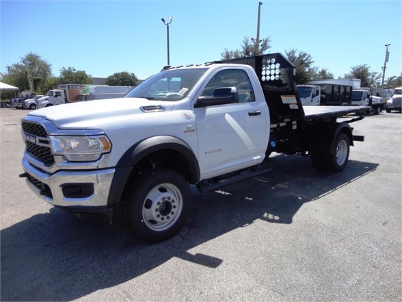 Ram 5500 HD hooklift truck showing flatbed and wheel wells, white cab, black equipment on rear, stock J74972.