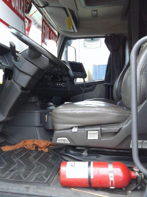 Volvo D13 truck interior showing driver's seat, dashboard, steering wheel, and a red fire extinguisher on the floor near the door.