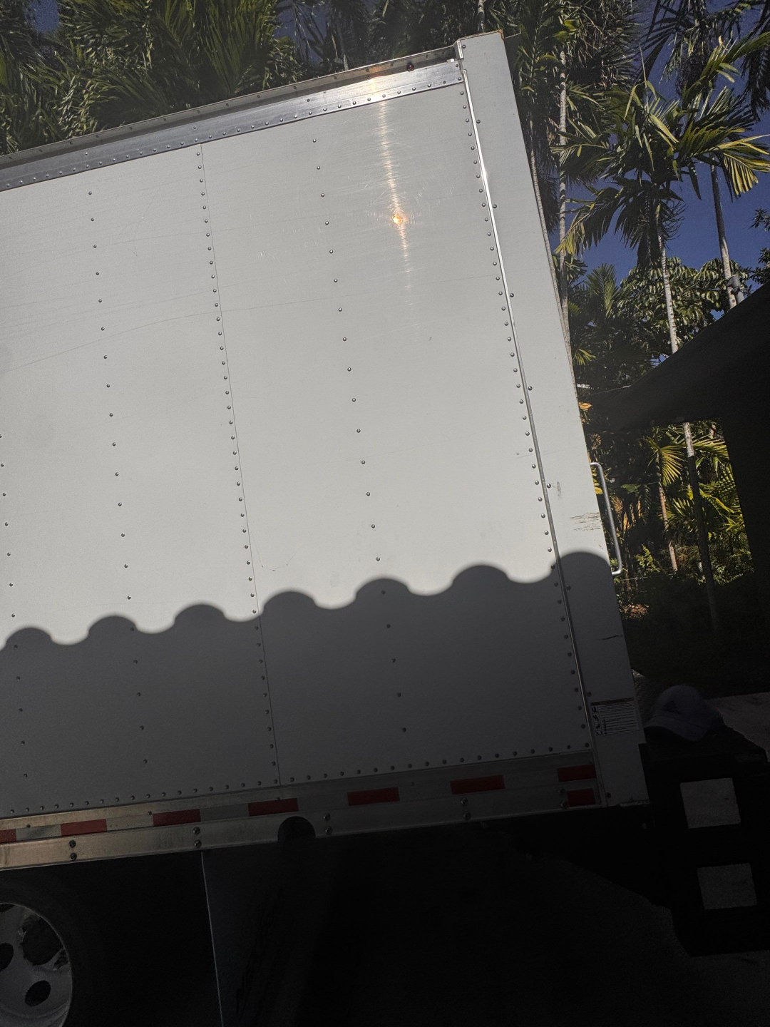 Isuzu box truck trailer side with riveted aluminum panels and shadow of person in foreground.