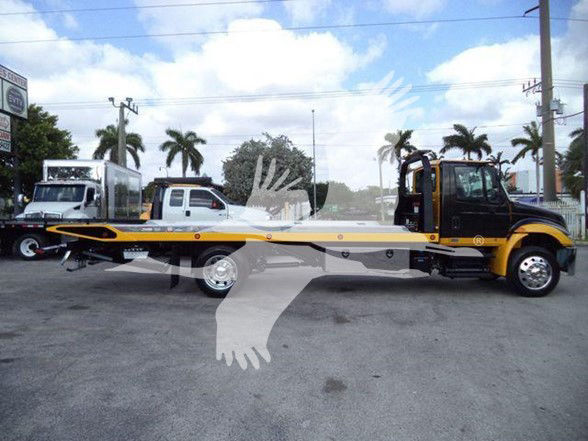 Tow truck integral side view showing International DURASTAR 4300 with flatbed, black and yellow cab, long yellow bed, and dual rear wheels.