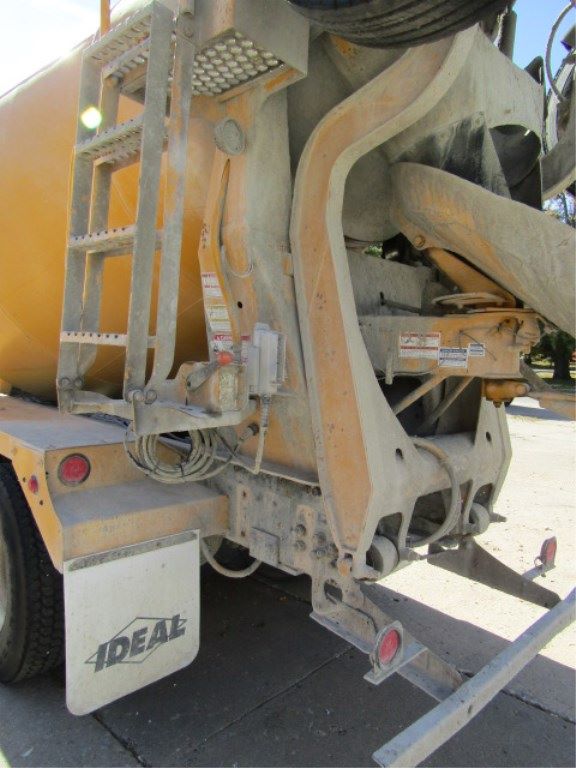 Concrete mixer truck rear end showing cement drum and chute, with IDEAL mud flaps, ladder, hydraulic components, and warning labels.