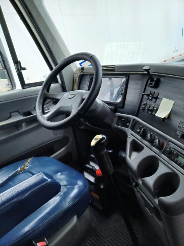 Truck interior showing steering wheel, dashboard with touchscreen, gear shifter, and blue seat in a Freightliner Columbia cab.