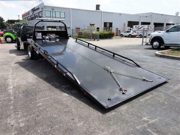 Ram 5500 tow truck flatbed with black steel ramp and chains in a dealership lot.