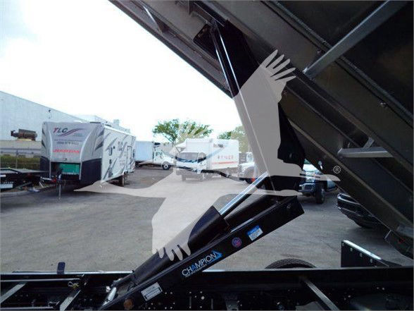 Isuzu NPR HD dump truck hydraulic system with arm and label; windshield view of truck bed in raised position; hydraulic cylinder with Champion branding.