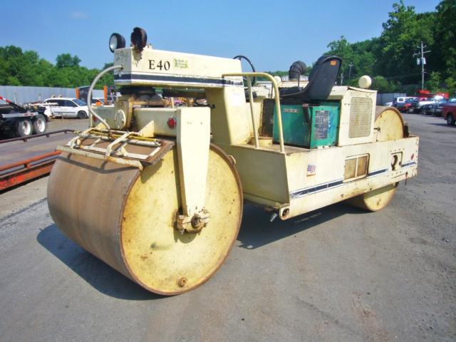 Trucking equipment: large front drum compactor with operator seat, E40 label, and beige/green paint. Side and rear view showing hydraulic and control housings.