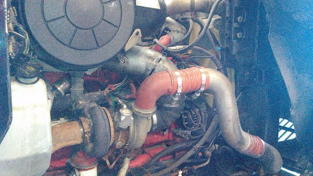 Truck engine bay with red intercooler hose, turbocharger, air intake, and various hoses and wires visible.
