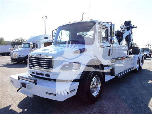 Freightliner BUSINESS CLASS M2 106 tow truck with crane arm on the rear, white paint, front bumper, chrome grille, dual headlights, side steps, and large mirrors.