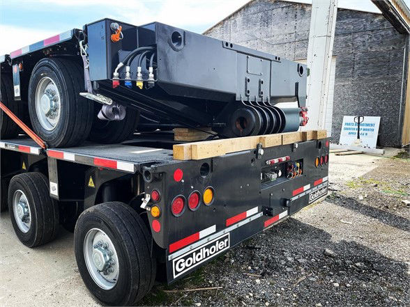 Goldhofer heavy-duty trailer in a dock area with a detached deck section loaded on the back. Visible rear lights, dual axles, tires, and safety reflectors. Branding shows Goldhofer.