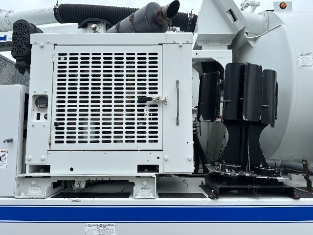 Freightliner 114SD vacuum truck side panel with radiator grille and engine bay, showing large white cabinet and black insulated hoses.
