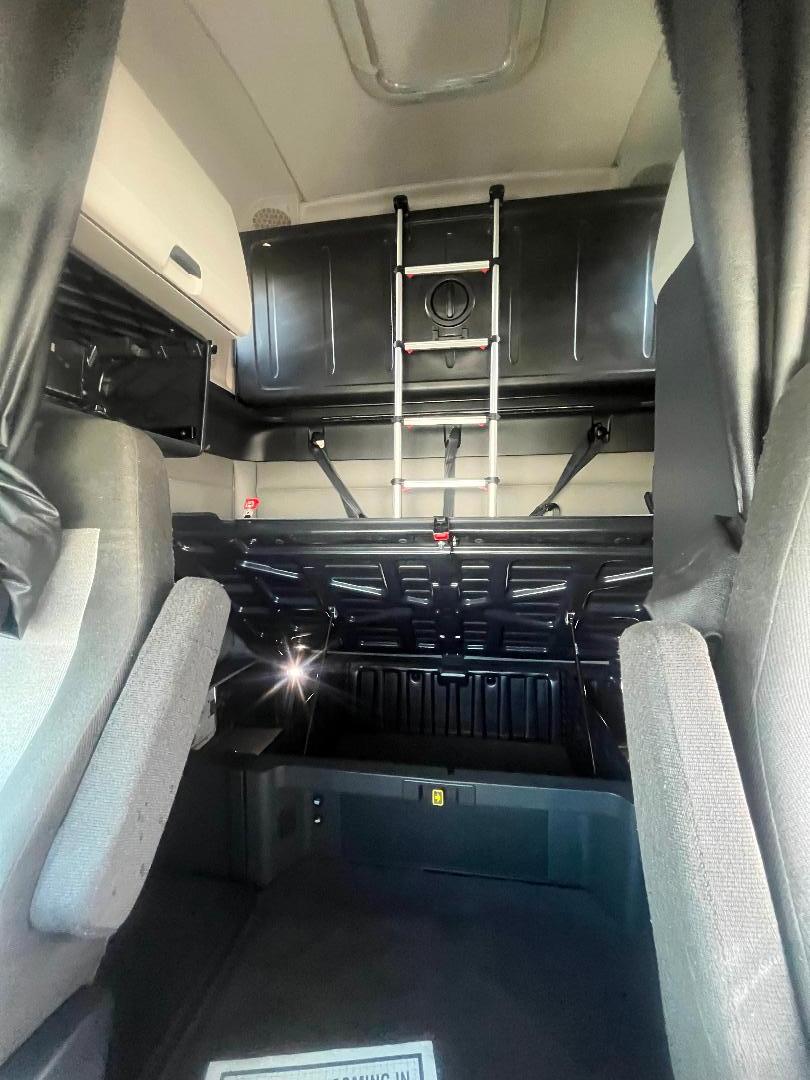 Cab interior of a 2021 Freightliner Cascadia 126 sleeper with ladder to upper bunk, storage cabinets, and seating visible.