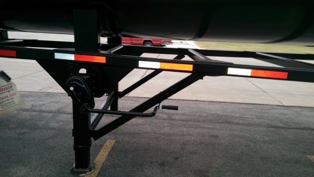 Trailer undercarriage showing part of tank and support legs with reflective orange/white safety strips.