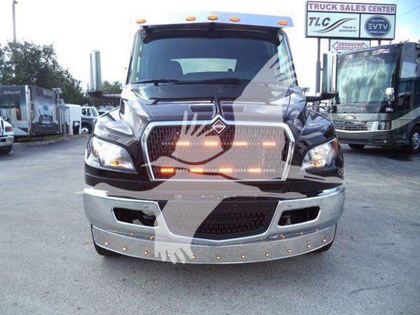 Front view of a 2024 International MV tow truck with illuminated amber lights and a chrome grille.