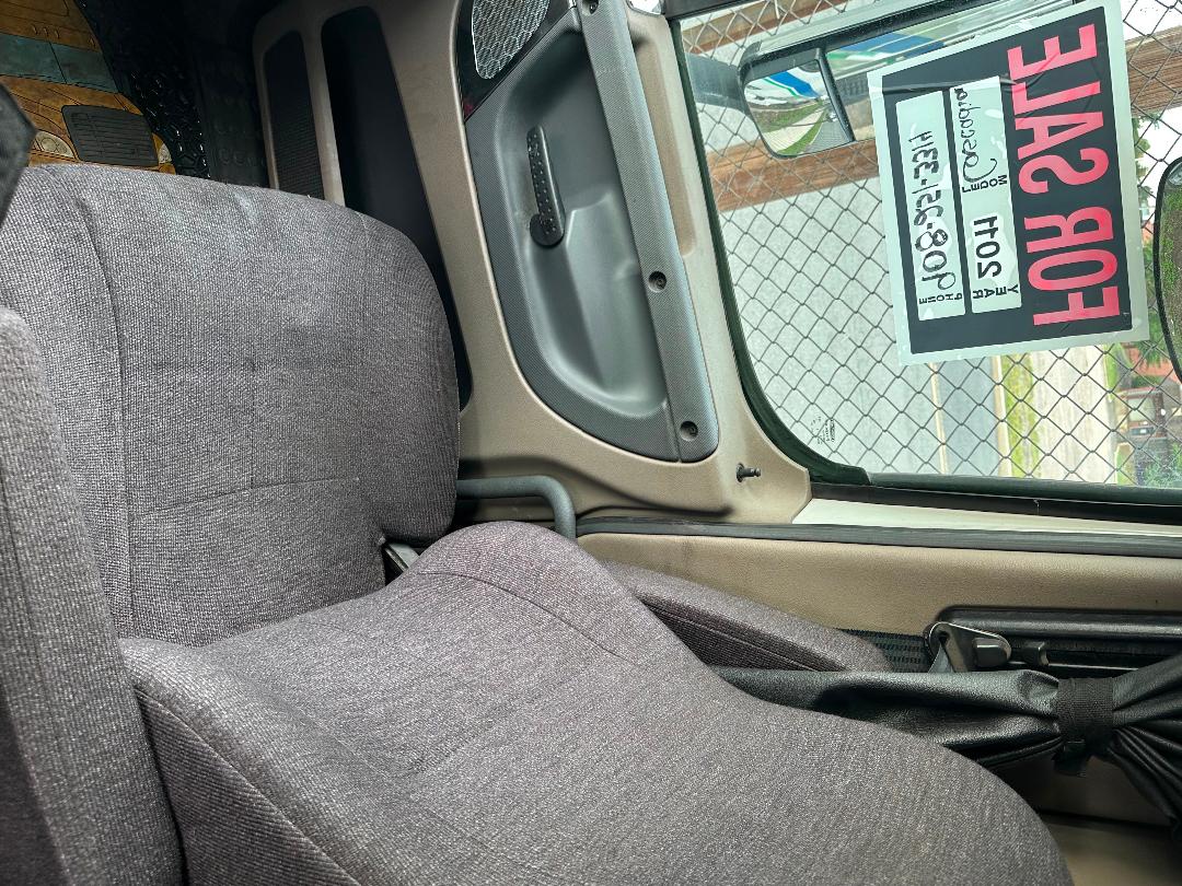 Cab interior of a 2011 Freightliner Cascadia tagged for sale, showing driver seat, window, and door panel with a 'FOR SALE' sign visible.