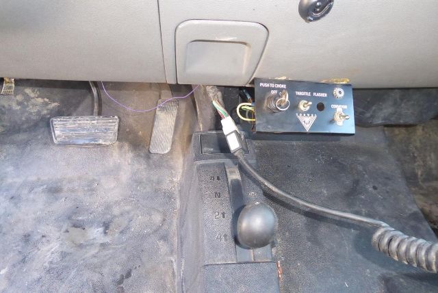 Inside cab floor of a 2011 Chevrolet 2500HD showing transmission gear shift lever, pedals (brake, accelerator), and a control panel with push-to-choke switch and wiring.