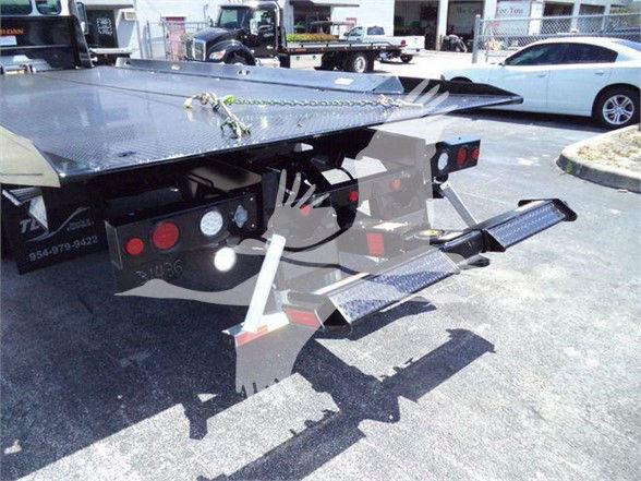 Tow truck rear with flatbed and hydraulic ramps, rear lights, and platform steps; visible metal diamond plate surface and undercarriage; no legible brand text visible on image.