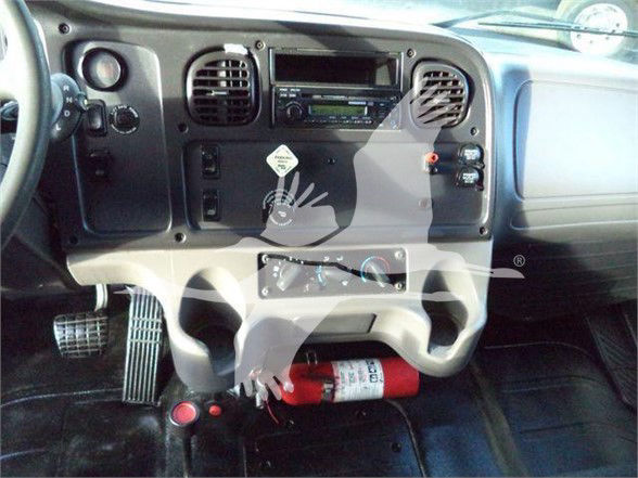 Dashboard of a 2012 Freightliner BUSINESS CLASS M2 106 showing steering wheel, center console, air vents, radio, controls, pedals, and a red fire extinguisher under the dashboard.