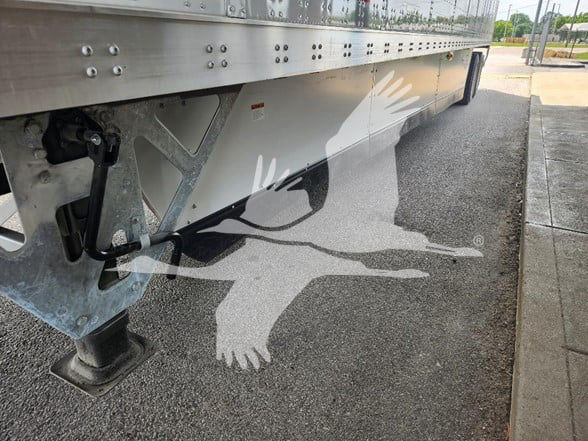 Trailer undercarriage with support jack and side skirt, showing underside hardware and a partial graphic of a flying bird across the side.
