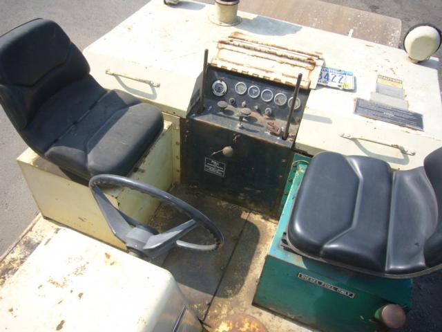 Trucking equipment cab with two seats and instrument panel, gauges, and control levers in view.
